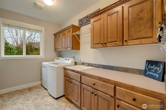 clothes washing area with cabinet space, baseboards, washing machine and dryer, and a sink