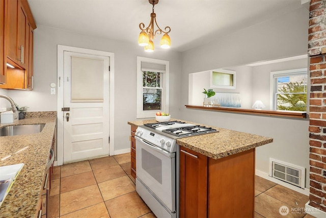 kitchen featuring light tile patterned floors, visible vents, gas range gas stove, a sink, and brown cabinets