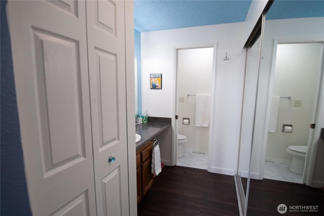 bathroom with vanity, toilet, baseboards, a textured ceiling, and wood finished floors