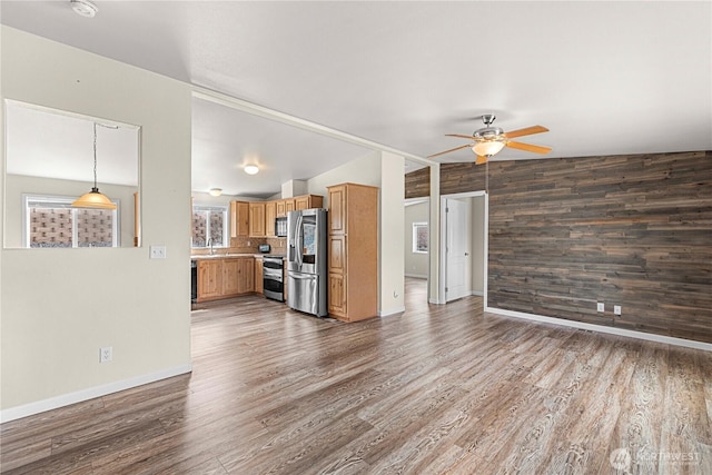 unfurnished living room with a ceiling fan, wood walls, lofted ceiling, and wood finished floors