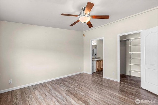 unfurnished bedroom featuring a closet, wood finished floors, a spacious closet, ensuite bathroom, and baseboards