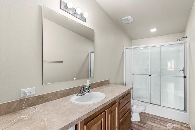 bathroom with a shower with shower door, toilet, vanity, and wood finished floors