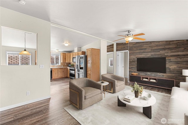 living area featuring vaulted ceiling, baseboards, an accent wall, ceiling fan, and wood finished floors