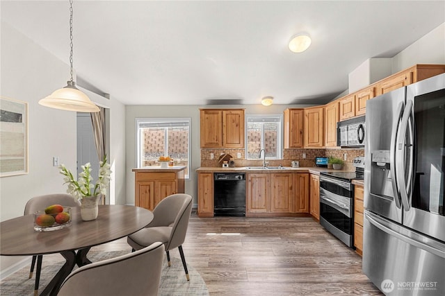 kitchen featuring decorative light fixtures, light wood-type flooring, backsplash, a sink, and black appliances