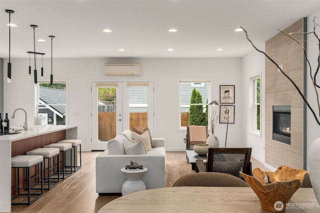 living area featuring a wall unit AC, light wood-type flooring, recessed lighting, a fireplace, and french doors