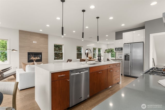 kitchen featuring stainless steel appliances, a sink, open floor plan, light wood-type flooring, and modern cabinets