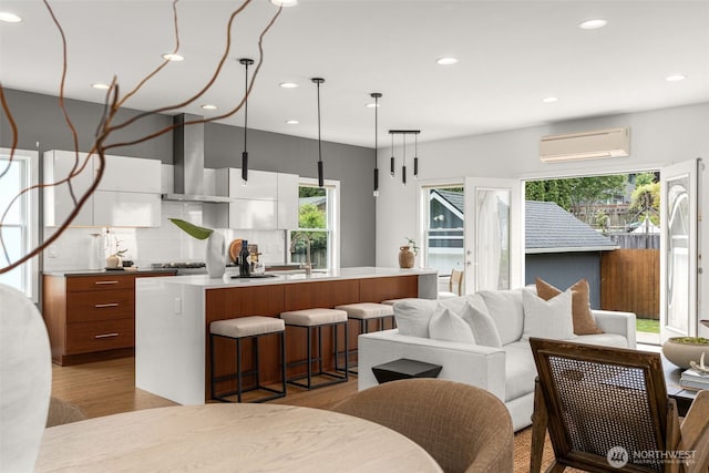 kitchen featuring wall chimney range hood, a wall mounted AC, modern cabinets, recessed lighting, and light countertops