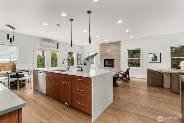 kitchen featuring open floor plan, a sink, stainless steel dishwasher, light wood-style flooring, and light countertops