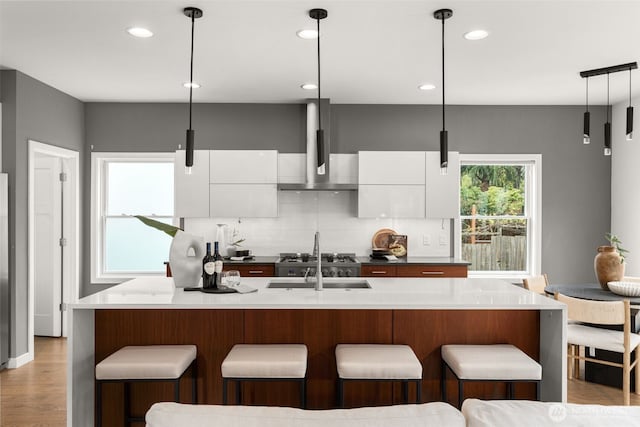 kitchen featuring wall chimney range hood, modern cabinets, decorative backsplash, white cabinets, and hanging light fixtures