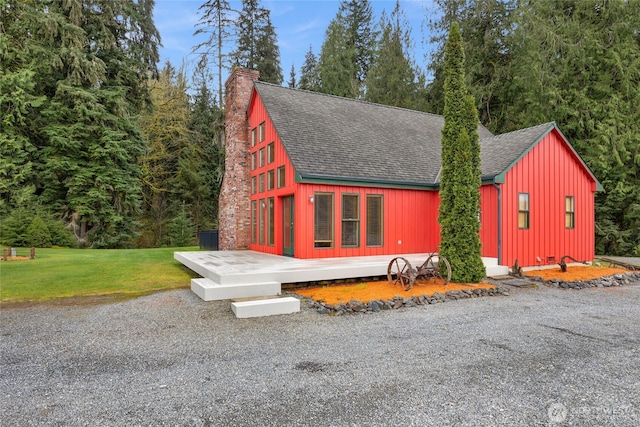 view of front facade featuring roof with shingles, a chimney, a wooden deck, and a front yard
