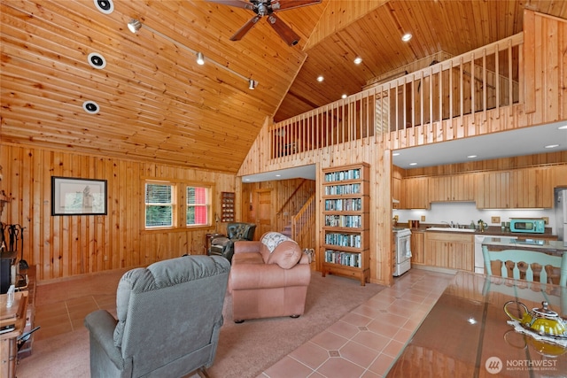 living room featuring light tile patterned floors, ceiling fan, a towering ceiling, wood ceiling, and wooden walls