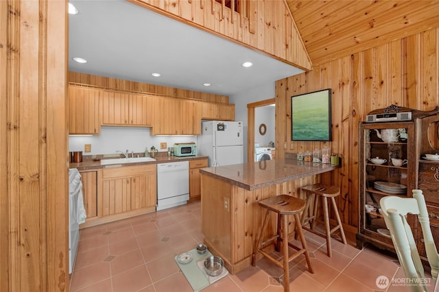 kitchen with white appliances, wooden walls, a peninsula, and light tile patterned flooring