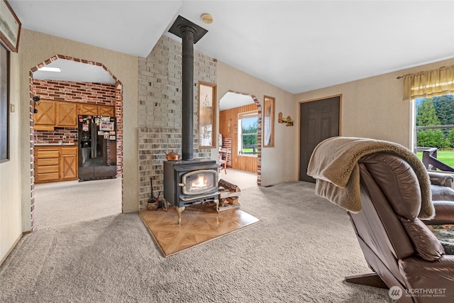 living area featuring a wood stove, arched walkways, light colored carpet, and lofted ceiling