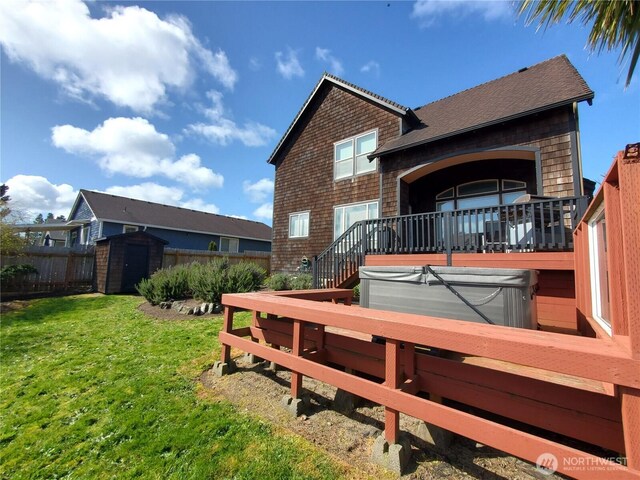 back of property with an outbuilding, fence, a covered hot tub, a storage unit, and a lawn