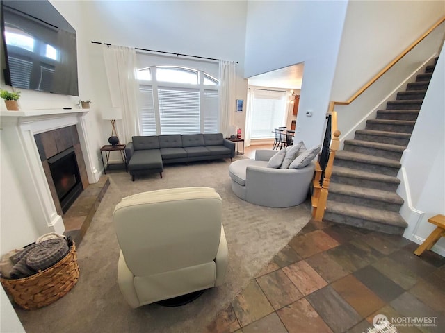 living area featuring stairs, a fireplace, and a high ceiling