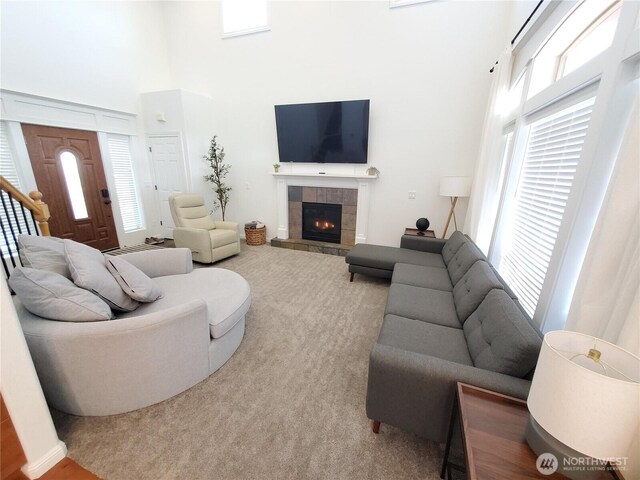 living room with carpet flooring, a towering ceiling, and a tile fireplace