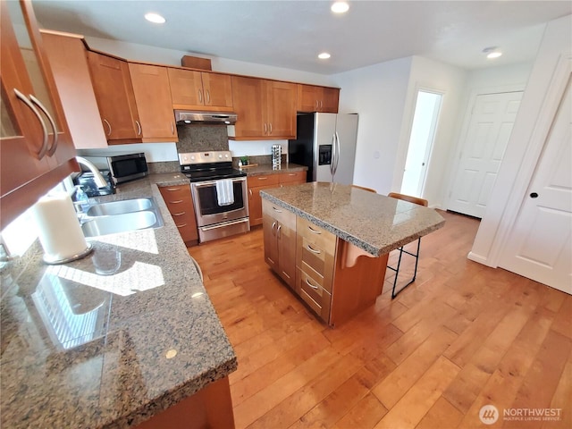kitchen featuring a sink, a kitchen bar, appliances with stainless steel finishes, light wood-type flooring, and under cabinet range hood