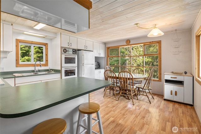 kitchen with white appliances, white cabinetry, a sink, light wood-style floors, and wooden ceiling