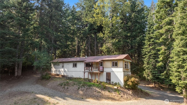 view of front of property featuring dirt driveway, metal roof, and a forest view