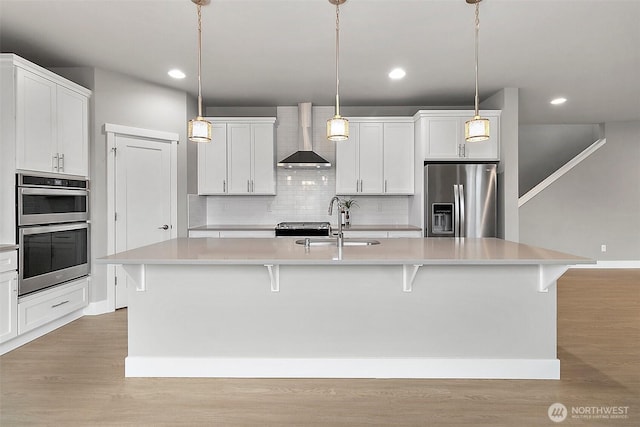 kitchen featuring light wood-type flooring, wall chimney range hood, a breakfast bar, appliances with stainless steel finishes, and backsplash