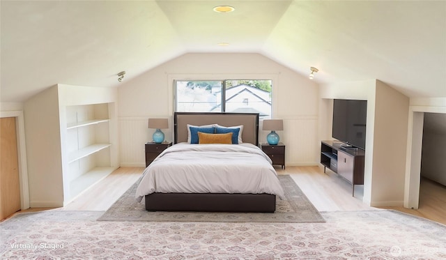 bedroom with light wood-style flooring, vaulted ceiling, and a wainscoted wall