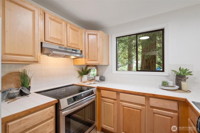 kitchen with backsplash, stainless steel range with electric stovetop, light brown cabinets, tile counters, and under cabinet range hood