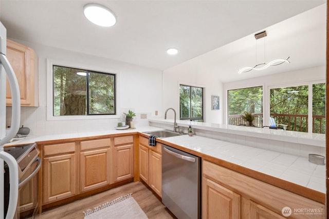 kitchen with tile counters, a sink, light wood-style flooring, hanging light fixtures, and stainless steel appliances