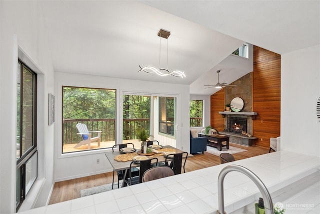 dining space featuring ceiling fan, a fireplace, wood walls, wood finished floors, and vaulted ceiling