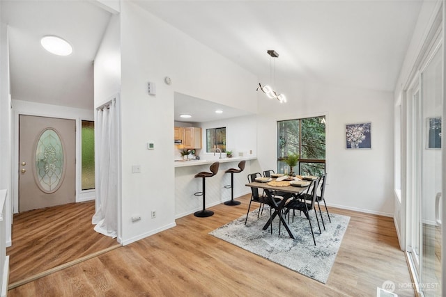 dining space with baseboards, vaulted ceiling, and light wood-type flooring