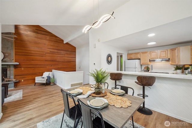 dining area with light wood-style floors, high vaulted ceiling, baseboards, and wooden walls