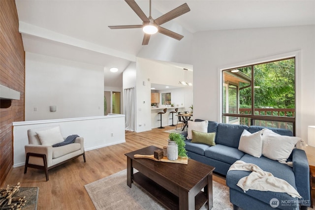 living area with a ceiling fan, baseboards, light wood finished floors, lofted ceiling, and wooden walls