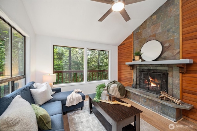 living room with wood walls, wood finished floors, a fireplace, high vaulted ceiling, and a ceiling fan