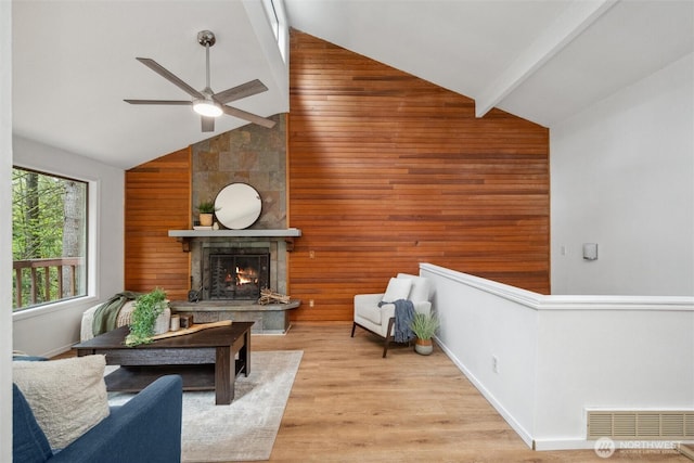 sitting room with ceiling fan, visible vents, a fireplace, high vaulted ceiling, and wooden walls