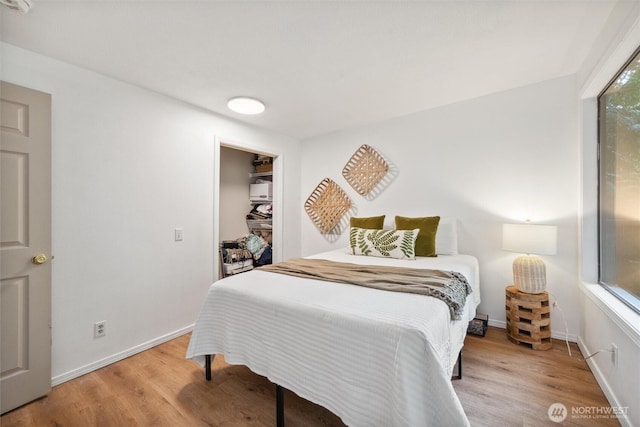 bedroom featuring baseboards, a walk in closet, and wood finished floors