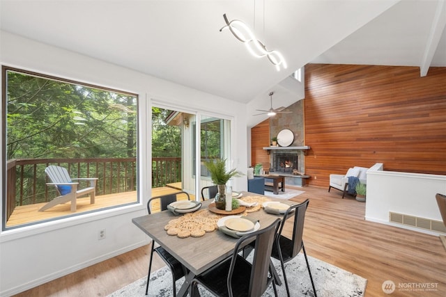 dining room featuring visible vents, wood walls, a stone fireplace, baseboards, and a ceiling fan