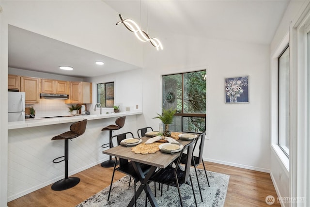dining space featuring baseboards, recessed lighting, light wood-style flooring, and a towering ceiling