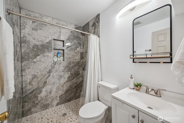 full bathroom with vanity, visible vents, toilet, and tiled shower