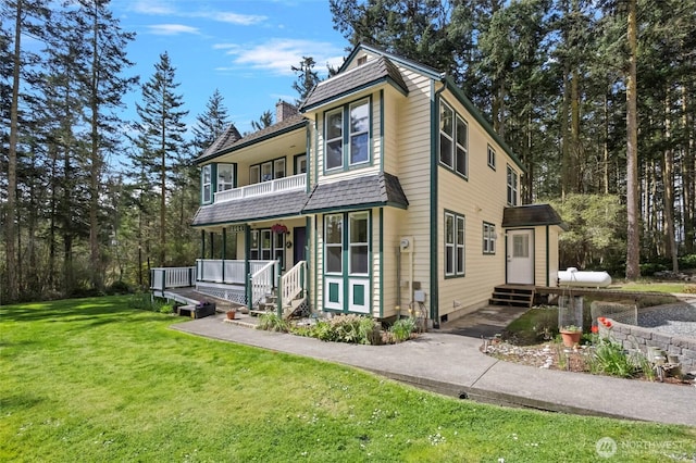 traditional home with covered porch, a chimney, a balcony, and a front yard