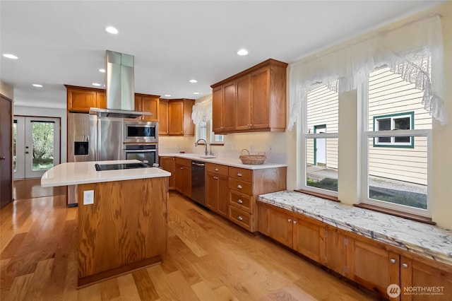 kitchen with light wood finished floors, stainless steel appliances, a sink, island range hood, and brown cabinetry