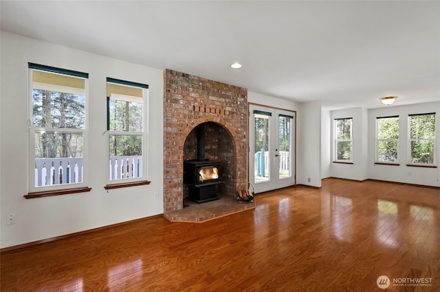 unfurnished living room with wood finished floors, a wood stove, baseboards, and french doors