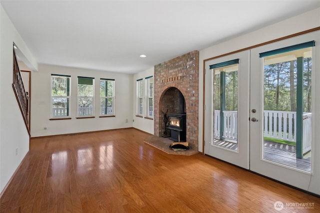 unfurnished living room with french doors, baseboards, wood finished floors, stairs, and a wood stove