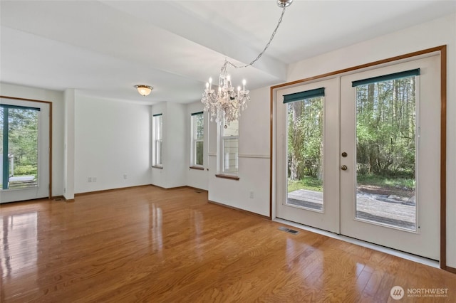 unfurnished dining area with wood finished floors, french doors, a notable chandelier, and plenty of natural light