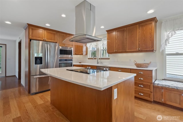 kitchen with light wood finished floors, brown cabinetry, island exhaust hood, and appliances with stainless steel finishes