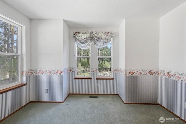carpeted empty room with visible vents and a wainscoted wall
