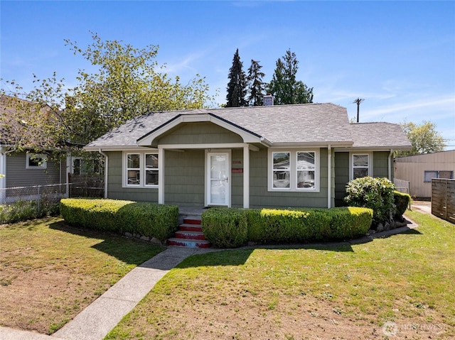 bungalow with a shingled roof, fence, and a front yard