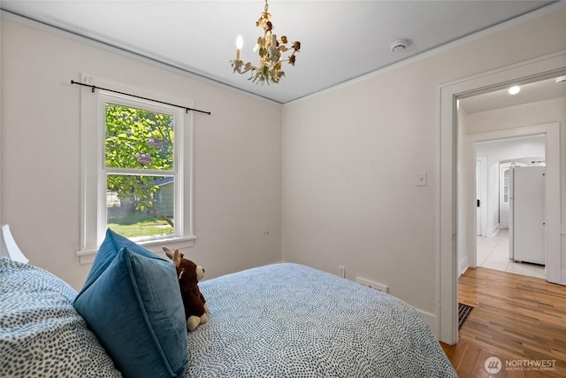 bedroom with light wood-type flooring, freestanding refrigerator, crown molding, and an inviting chandelier