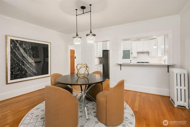 dining area featuring light wood finished floors, baseboards, crown molding, and radiator