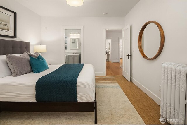 bedroom featuring light wood-style floors, radiator heating unit, baseboards, and ensuite bathroom