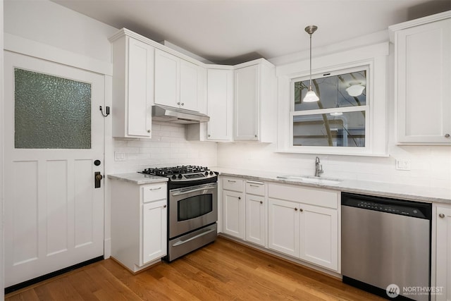 kitchen with white cabinets, under cabinet range hood, stainless steel appliances, light wood finished floors, and a sink