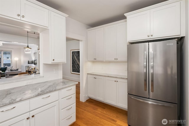 kitchen with pendant lighting, freestanding refrigerator, white cabinetry, light stone counters, and light wood finished floors
